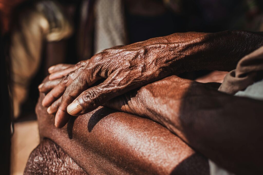 Detailed close-up of elderly hands resting on legs, highlighting aged skin and wrinkles.