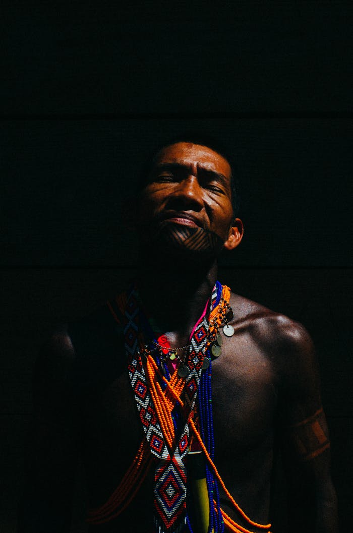 Man with colorful necklaces and tribal tattoos posing against a dark background in Panama.