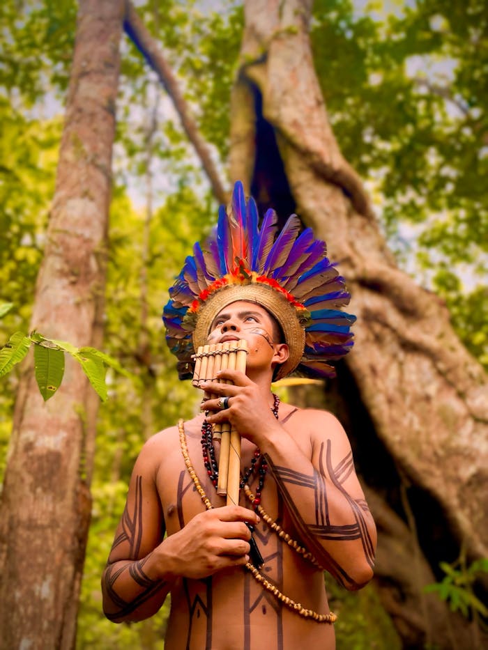 An indigenous man with a feather headdress playing a traditional flute in a lush forest.